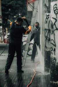 Workers cleaning graffiti off city building facade with a pressure hose.